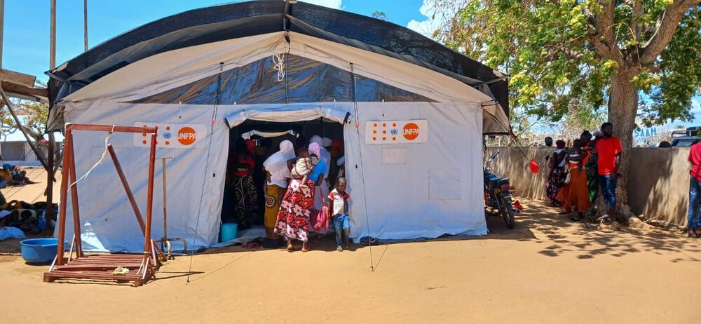 A group of women stand in line to enter a health facility with UNFPA branding.