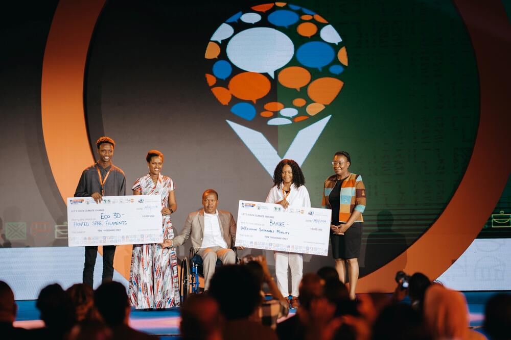 Innovation Hacklab winners stand in the stage with big checks in their hands. Lydia Zigomo, UNFPA ESA Regional Director stands with them.