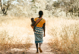 A girl carrying a baby walks down a path.