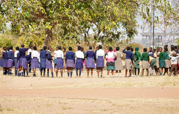 A group of young women stand in an open field talking. 