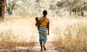 A girl carrying a baby walks down a path.