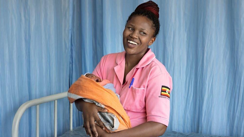 Inside of a hospital Edinah, a midwife, holds a baby. 