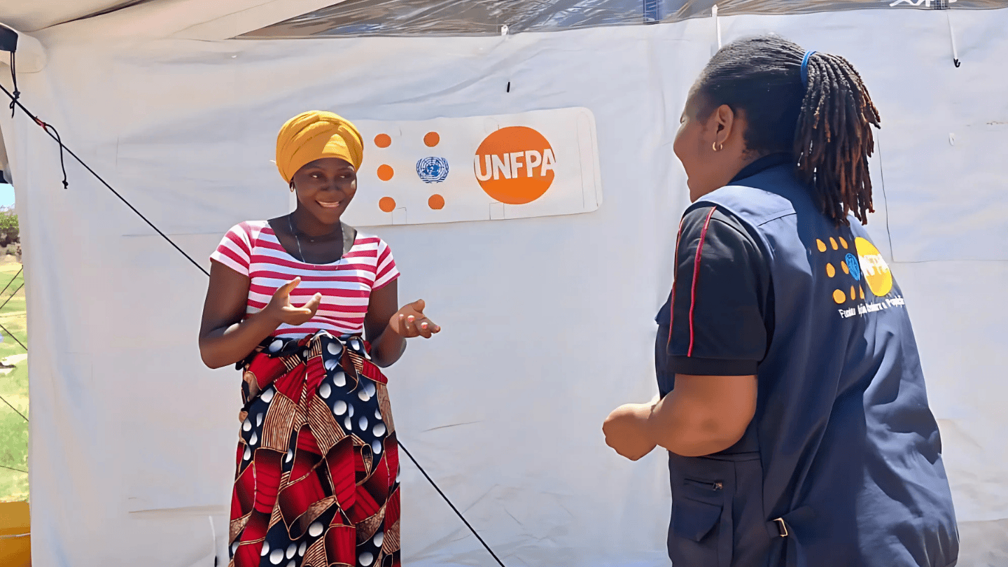 A pregnant woman talks with a woman wearing a UNFPA vest in front of a mobile clinic.