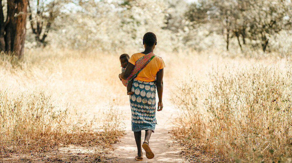 A girl carrying a baby walks down a path.