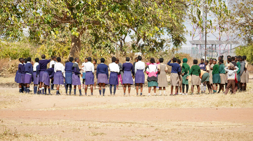 A group of young women stand in an open field talking. 